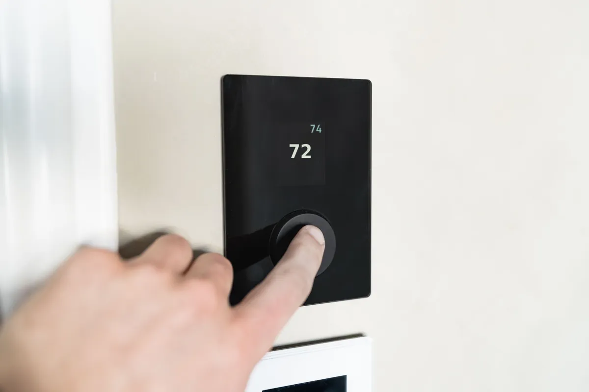 Homeowner adjusting a wall thermostat set to 72 degrees